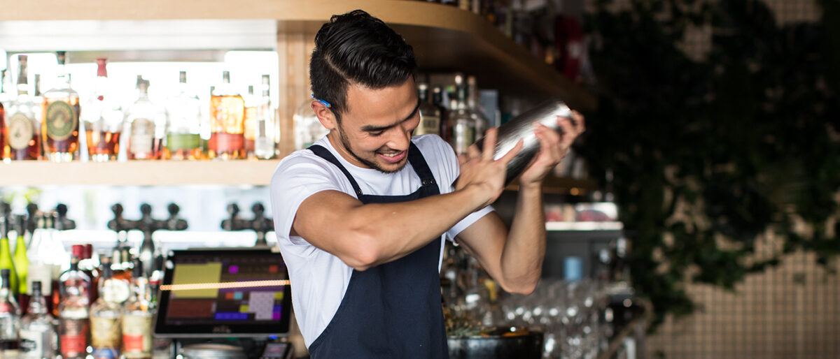 Friendly bartender smiling and shaking a cocktail