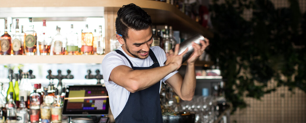 Friendly bartender smiling and shaking a cocktail